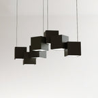 A Clérachic black cube chandelier against a pale wall, the cubes linked in an uneven row with lit undersides.