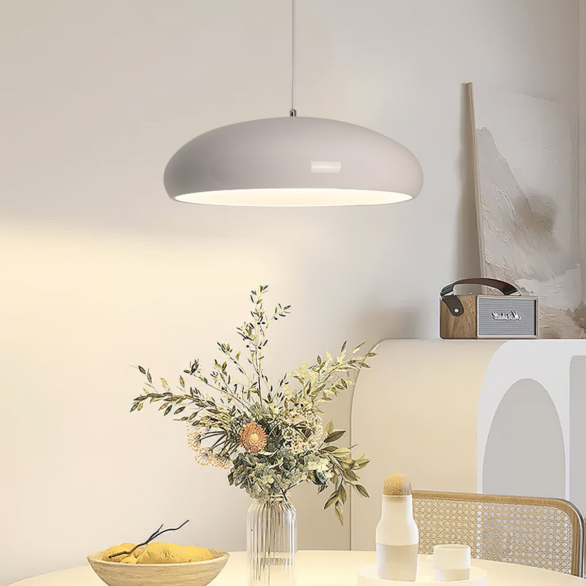 Pale grey Clérachic pendant glowing over a round table set with a vase of dried stems, a bowl of lemons and a cane-backed chair.