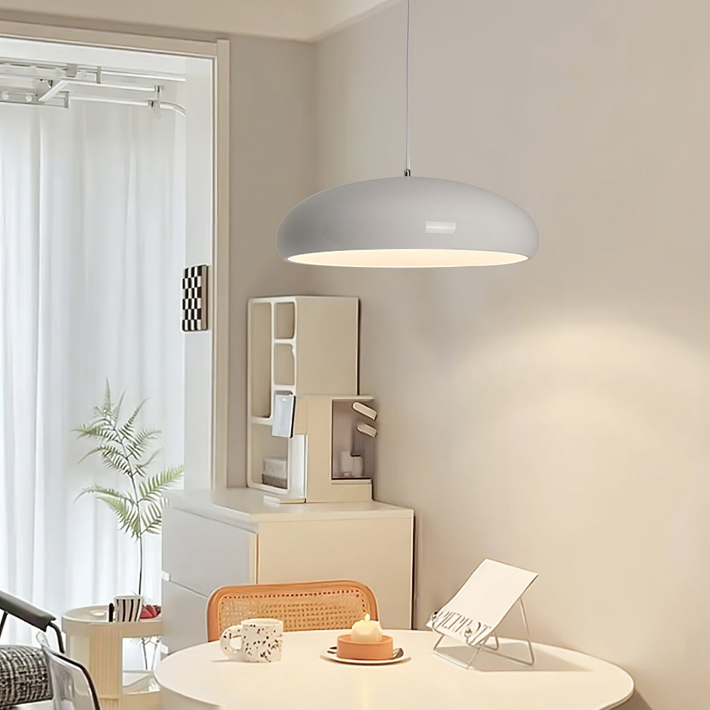 A light grey Clérachic dome pendant above a small round table in a bright corner, with a white shelf unit and a potted fern behind.