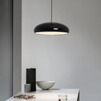 Black Clérachic dome pendant against a pale grey wall, with a dark vase and a stone bowl on the white table below.