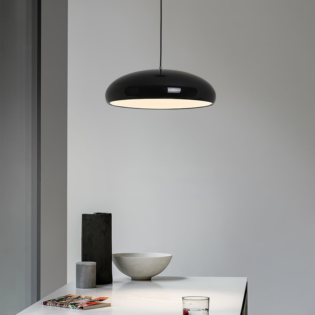 Black Clérachic dome pendant against a pale grey wall, with a dark vase and a stone bowl on the white table below.