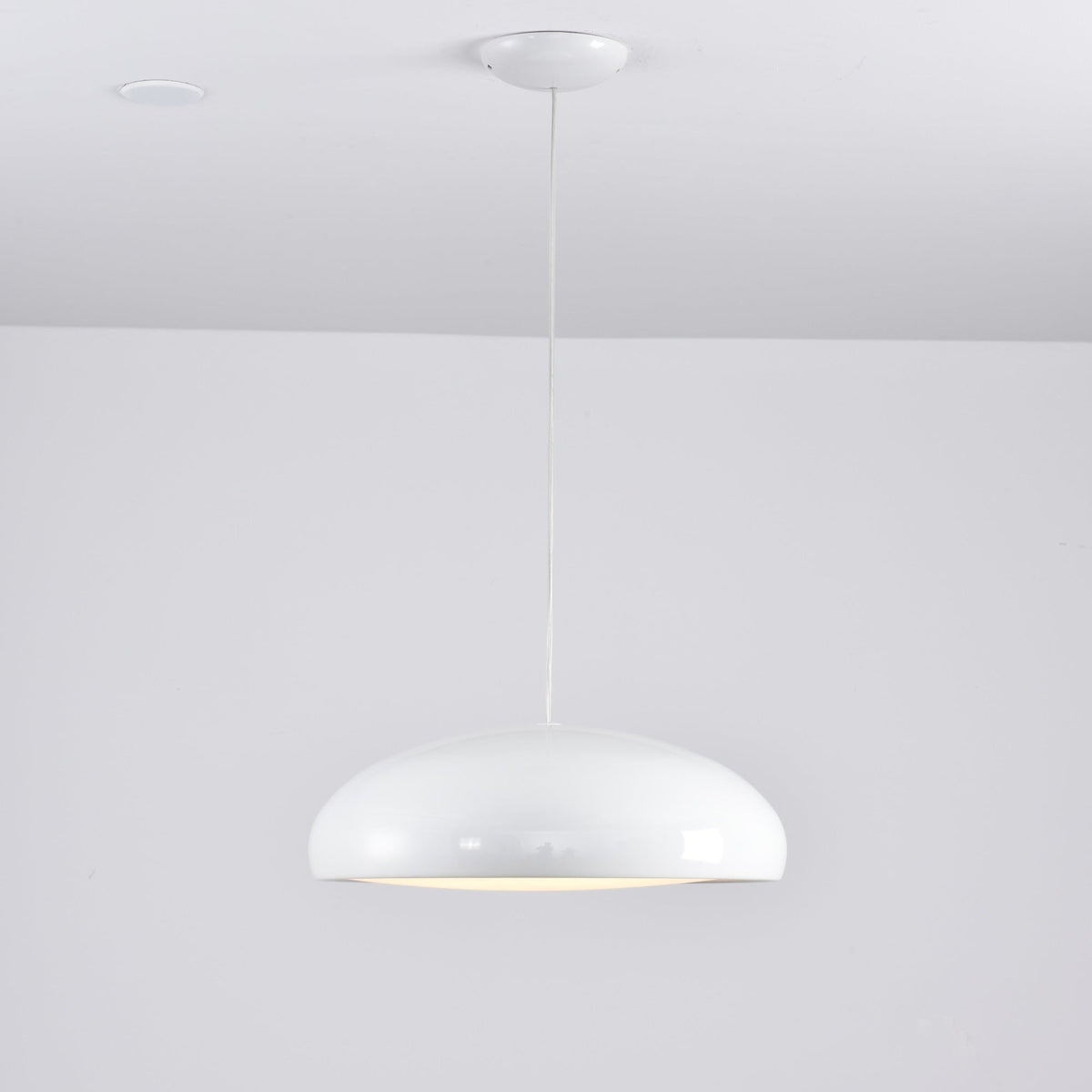 Small white Clérachic dome pendant on a long cable, with a white ceiling canopy and a soft glow at its base.