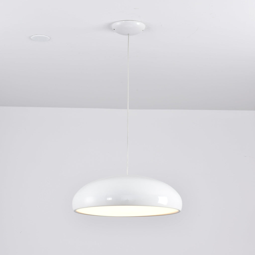 White Clérachic dome pendant glowing under its rim, hung from a white canopy beside a ceiling spotlight.