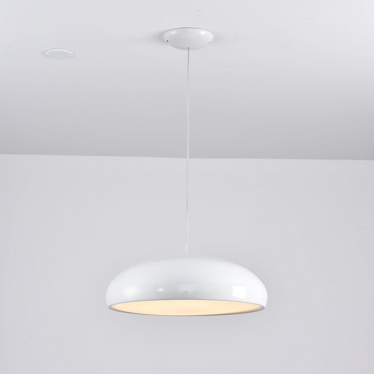 Glossy white Clérachic dome pendant lit from below, with a bright diffuser and a rounded white canopy above.
