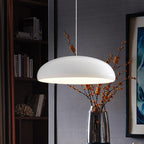 White Clérachic dome pendant beside a glass vase of orange berry stems, in front of a bookcase and a blue painting.