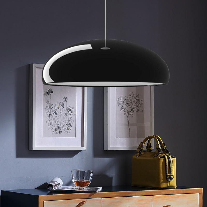 Close view of a gloss black Clérachic dome pendant, its curved shell catching the light above a sideboard and two framed prints.