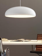 A white Clérachic dome pendant on a taupe wall, with its warm underside glow falling toward a white desk and an open book.