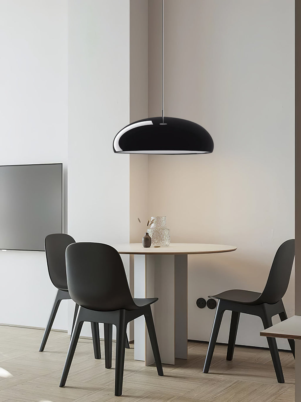 Small black Clérachic dome pendant above a round pedestal table with dark chairs, in a bright room with a pale wooden floor.