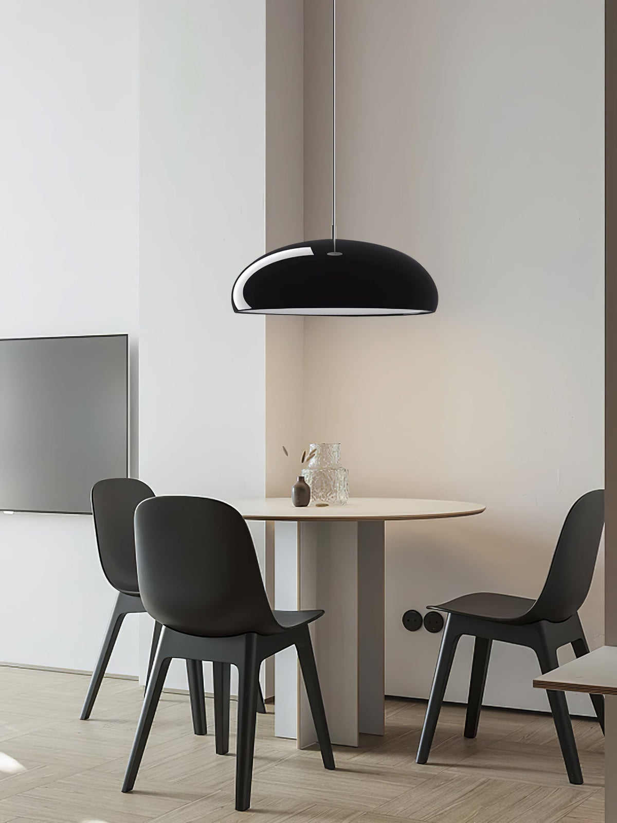Small black Clérachic dome pendant above a round pedestal table with dark chairs, in a bright room with a pale wooden floor.