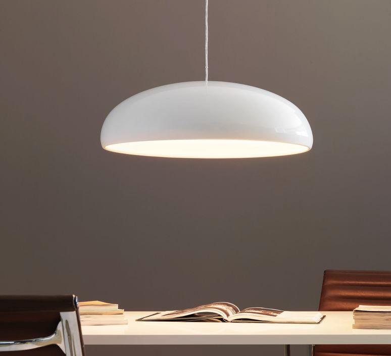 White Clérachic pendant with a warm lit underside, seen against a taupe wall above a white desk stacked with books.