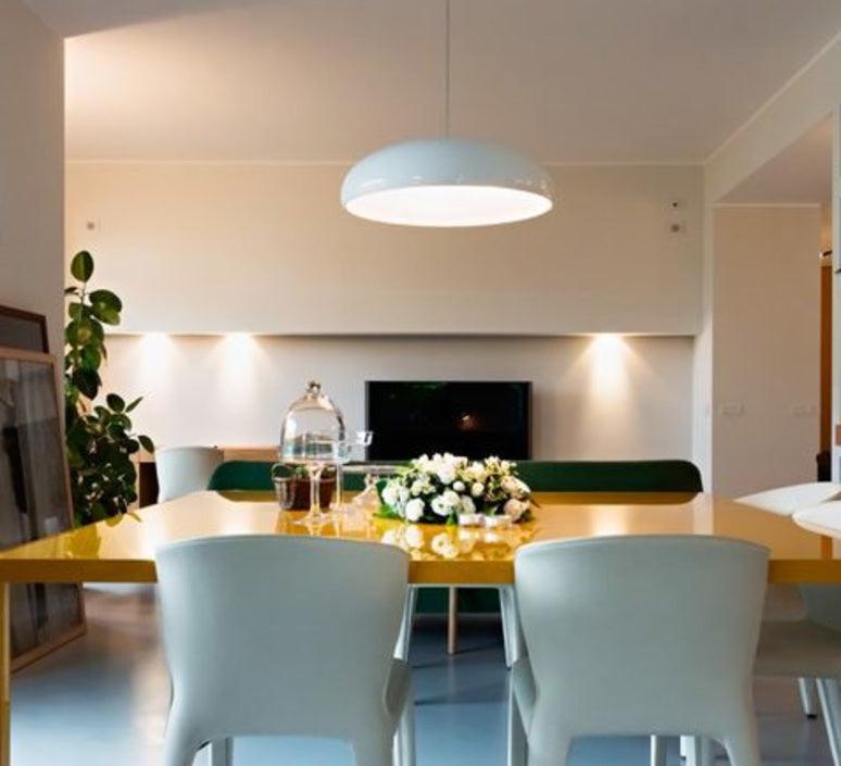 White Clérachic dome pendant hanging over a yellow-topped dining table with pale chairs, in an open-plan room with spotlights.