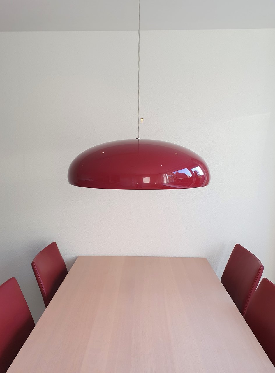 Dark-red Clérachic dome pendant over a pale wooden table, with dark-red chairs and a plain white wall in the background.