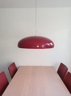 Dark-red Clérachic dome pendant over a pale wooden table, with dark-red chairs and a plain white wall in the background.