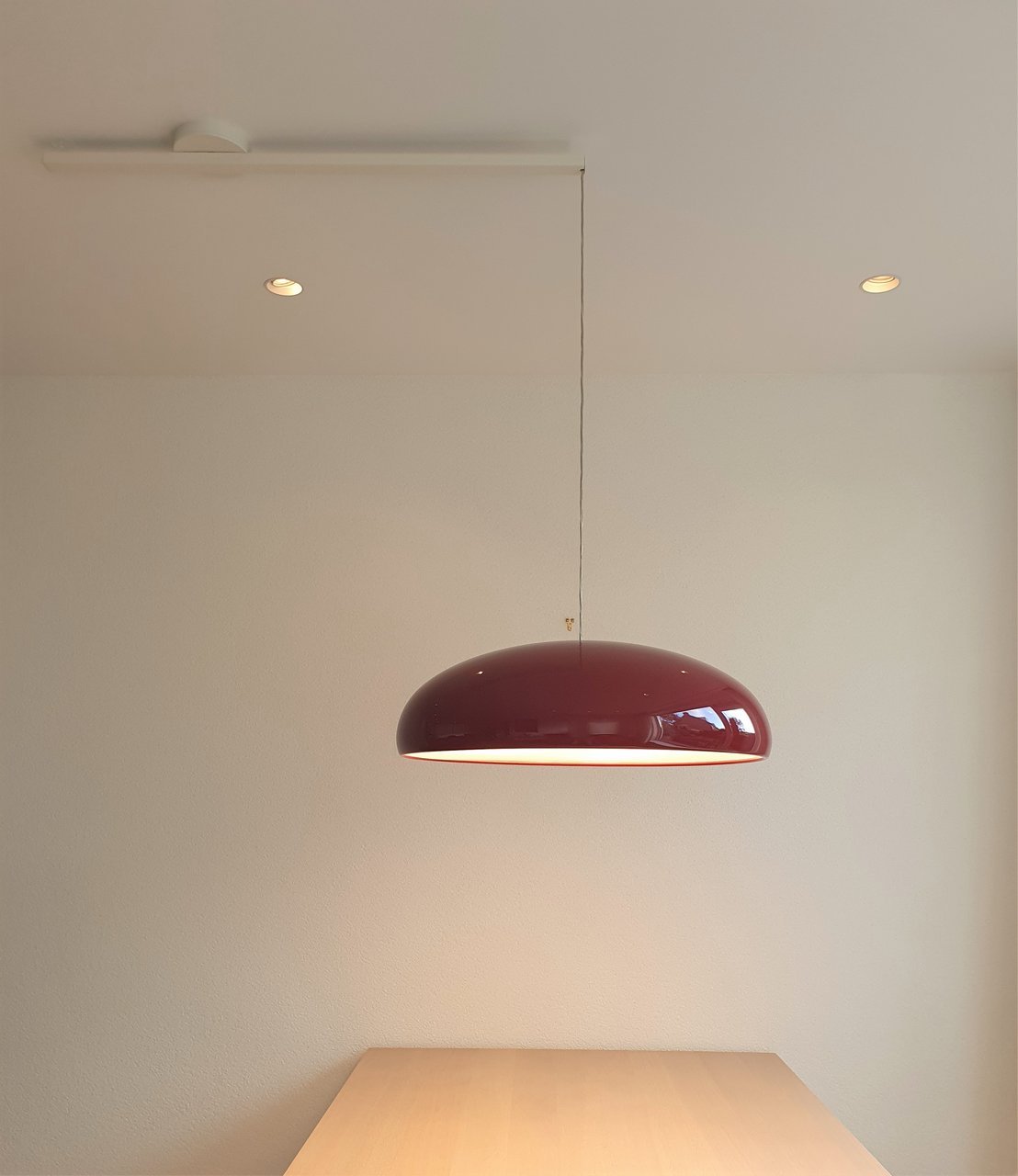 A smaller view of a dark-red Clérachic dome pendant hanging from a long cable above a pale wooden table.