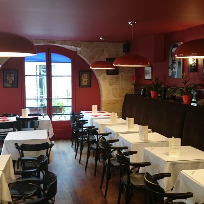 Several dark-red Clérachic dome pendants lit over a long row of tables in a restaurant with red walls and a stone arch.