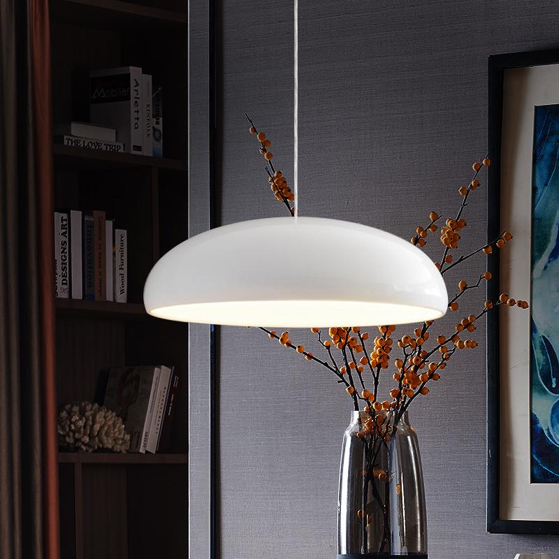 A white Clérachic dome pendant beside a glass vase of berry stems, with a bookcase and a blue painting in a dark study.