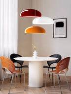 Three Clérachic dome pendants, dark red, white and orange, hung at staggered heights above a round white table and four chairs.