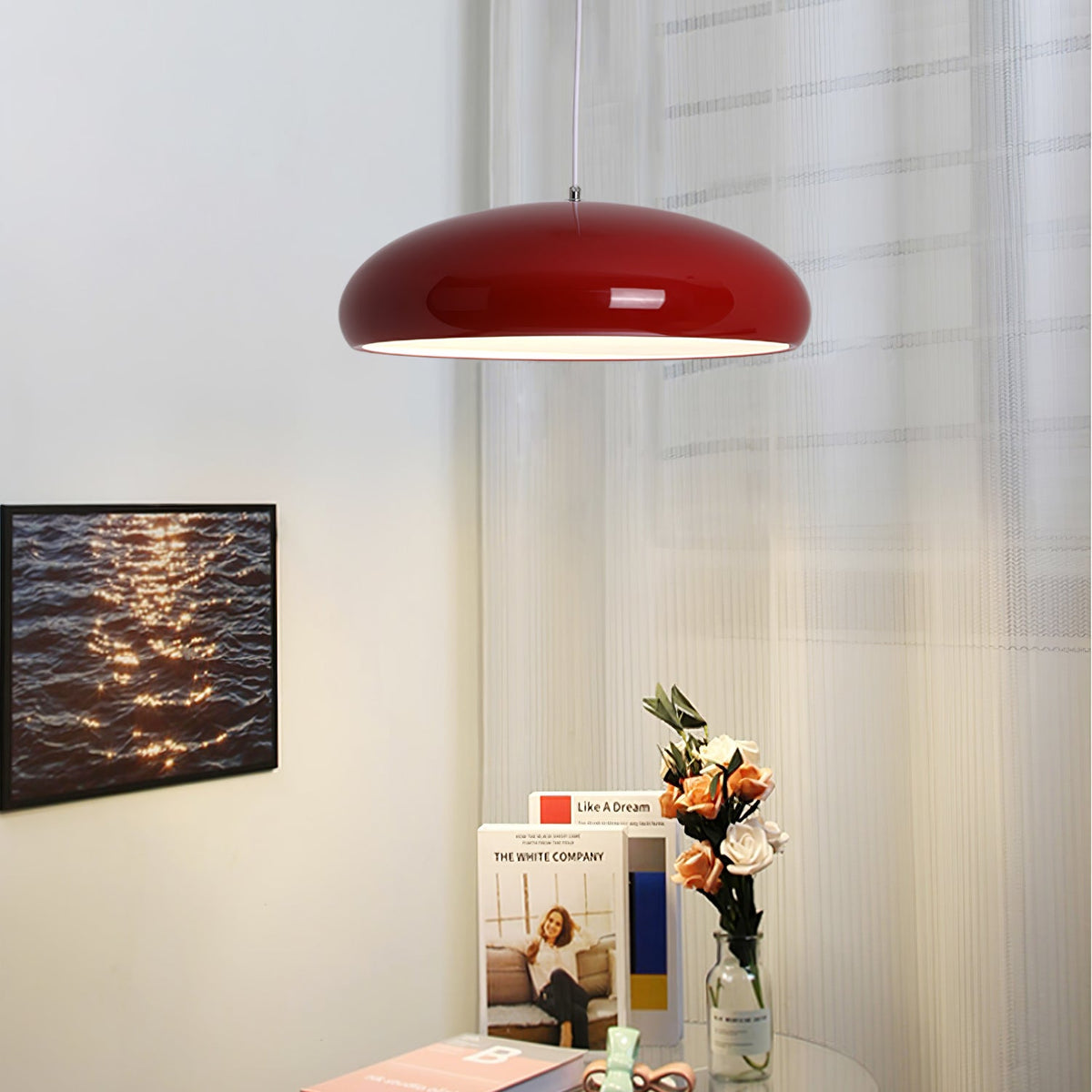 Dark-red Clérachic dome pendant beside sheer curtains, with a framed photograph of rippling water and a bunch of flowers below.