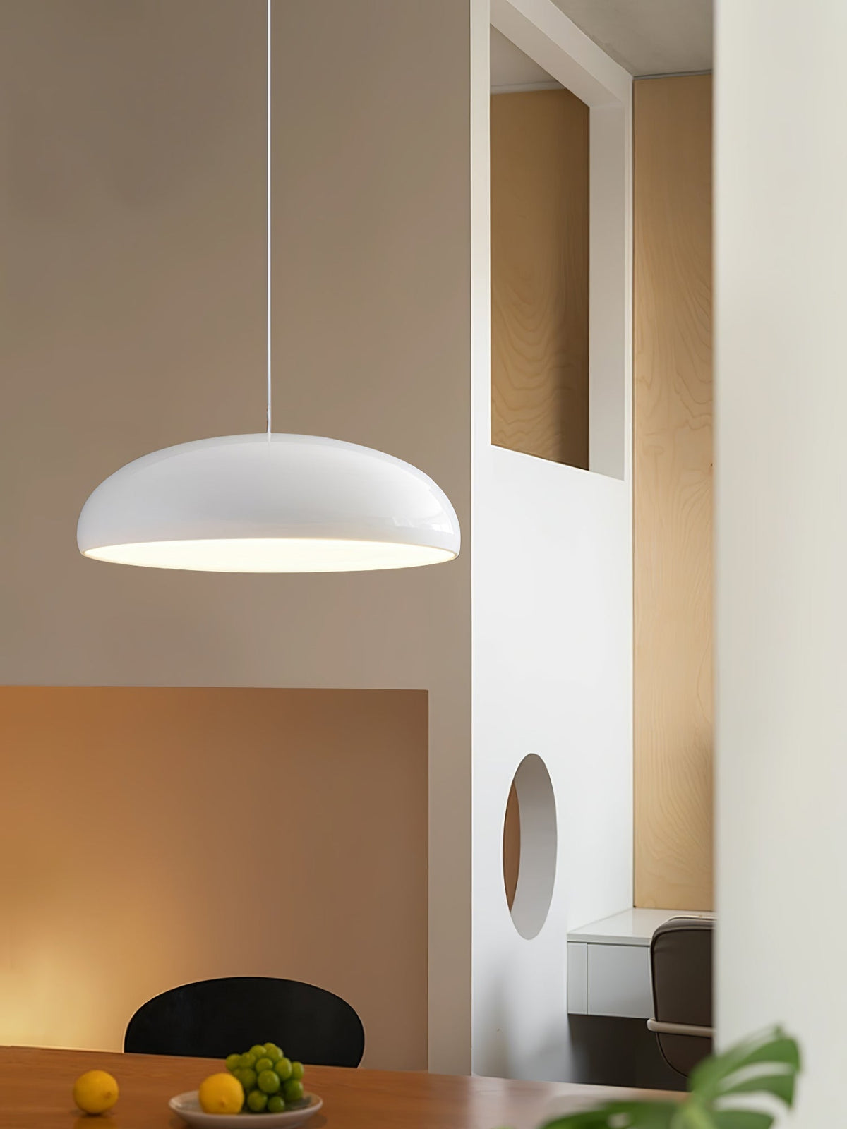 White Clérachic dome pendant glowing in a warm room with an arched wall opening, a black chair and a dish of fruit.