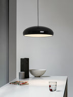 Black Clérachic dome pendant against a pale wall, above a white table with a stone bowl, a dark vase and a glass of water.