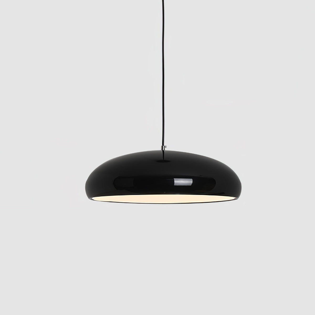 Close view of a black Clérachic dome pendant on grey, its glossy shell and warm white interior light both clear.