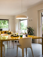 Cream-white Clérachic dome pendant hanging in a bright, open-plan room with a yellow dining table and green views outside.