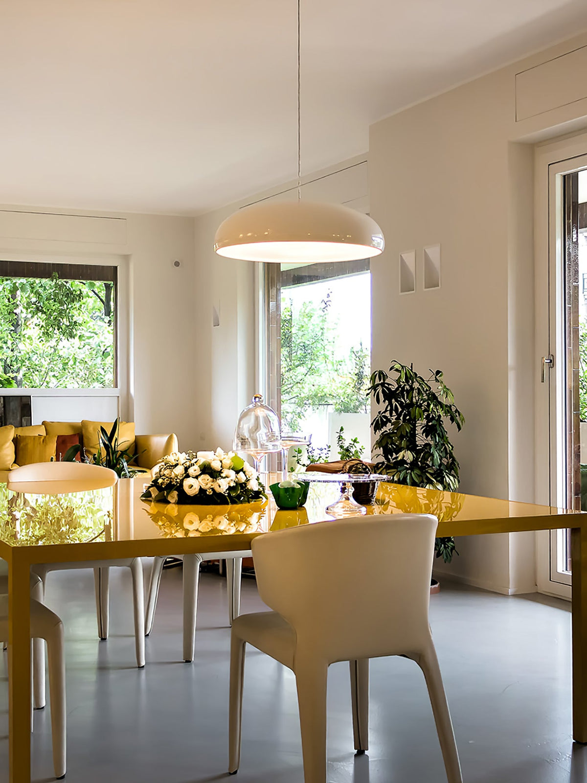 Cream-white Clérachic dome pendant hanging in a bright, open-plan room with a yellow dining table and green views outside.