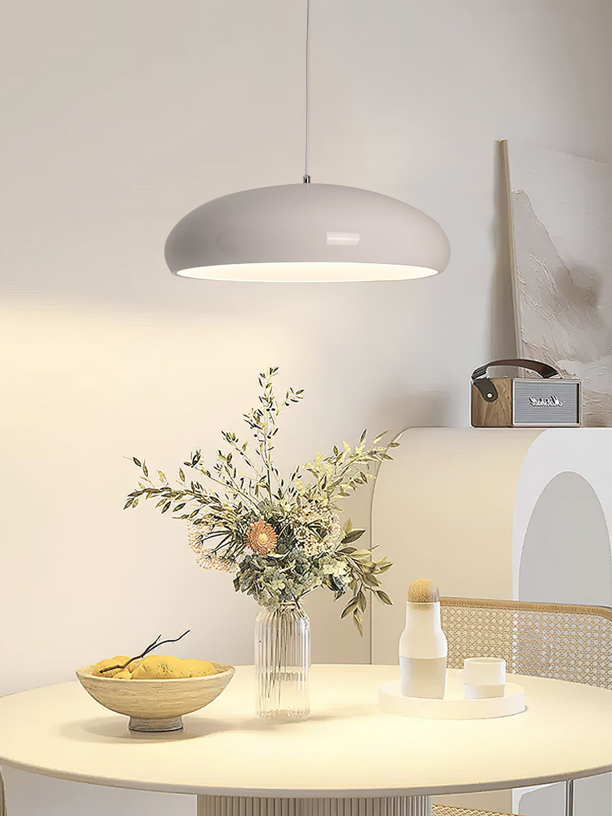 Light grey Clérachic dome pendant above a round table with dried flowers, a fruit bowl and a small vase against a cream wall.