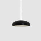 A black Clérachic dome pendant on a grey backdrop, hung from a thin black cable with its inner light glowing.