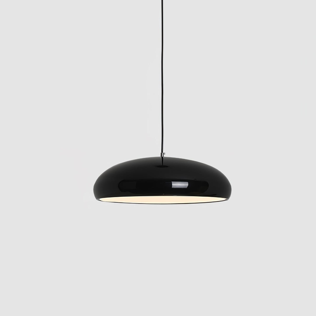 A black Clérachic dome pendant on a grey backdrop, hung from a thin black cable with its inner light glowing.