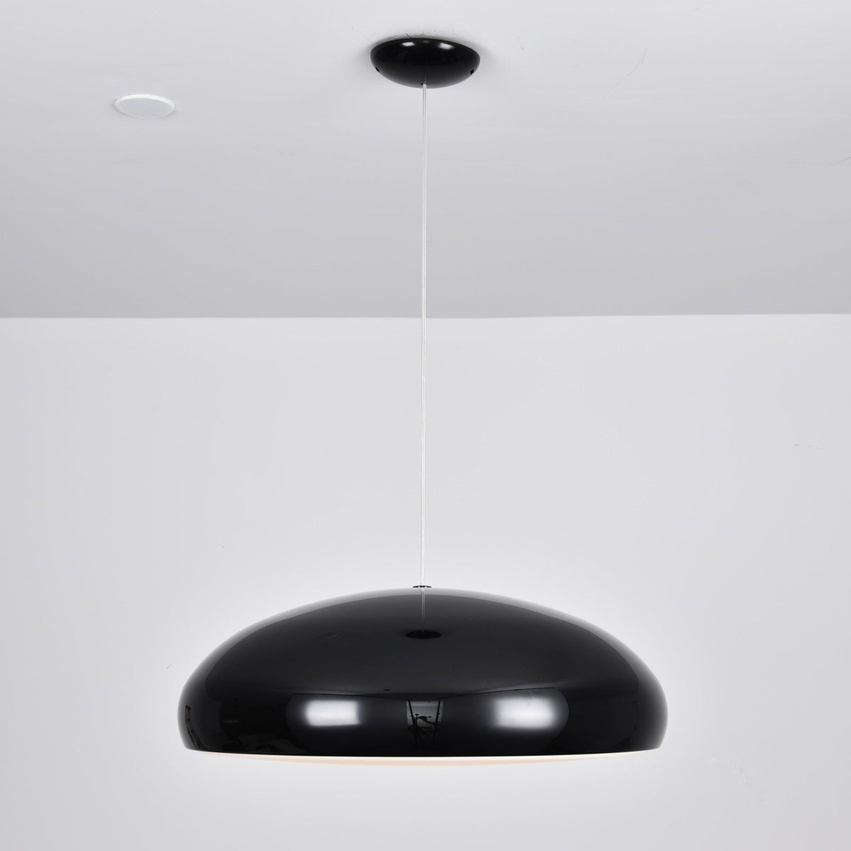 Wide, glossy black Clérachic dome pendant hung low from a black round canopy against a white wall.