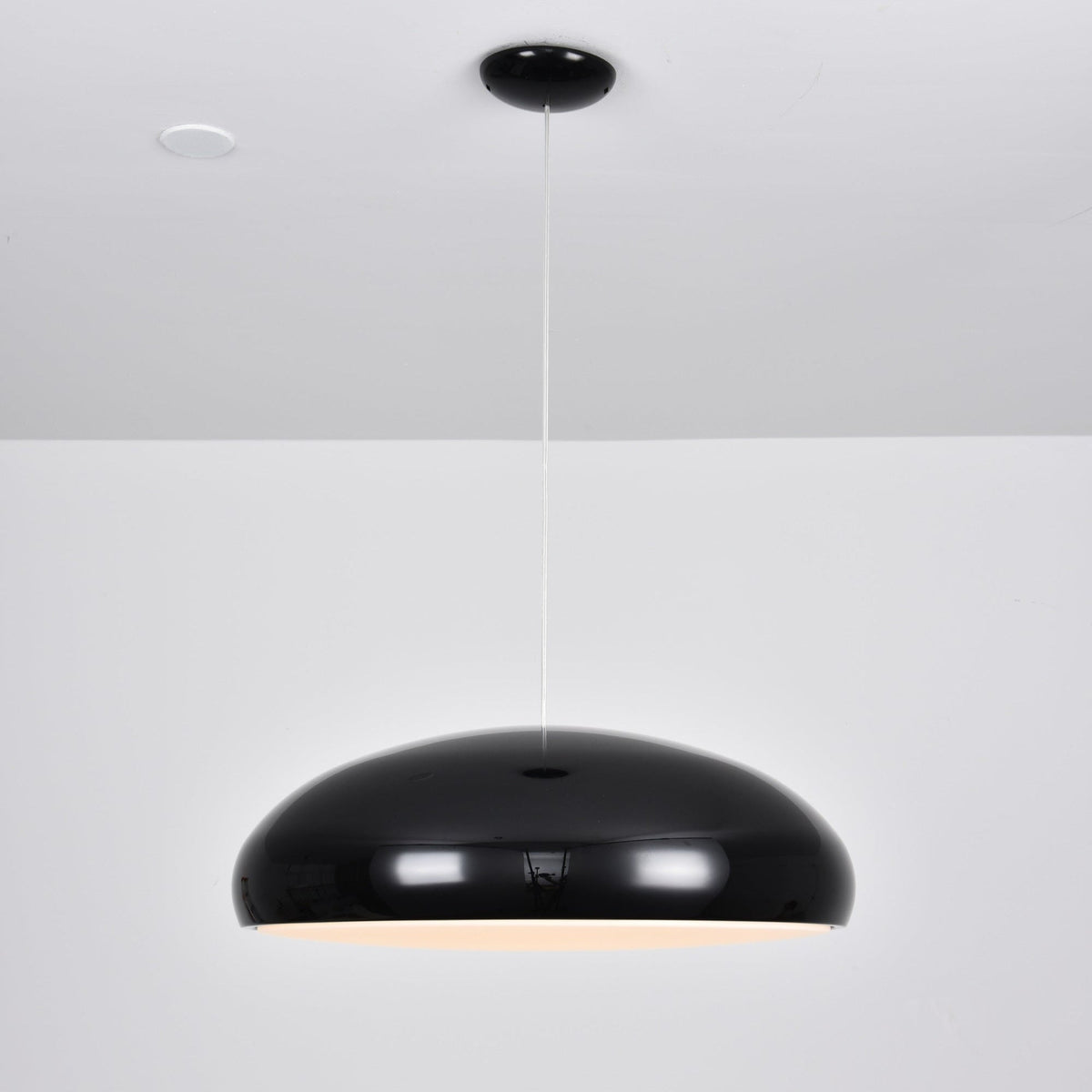 Black Clérachic dome pendant, side view, with a soft warm glow just visible under the shell and a spotlight overhead.