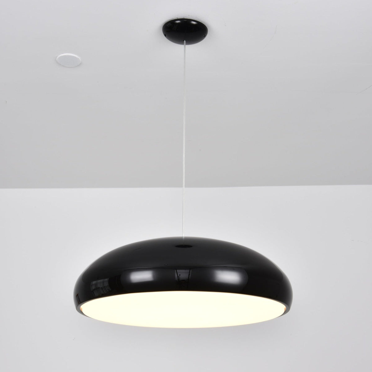Black Clérachic dome pendant lit from below, with a bright warm diffuser visible under the shell.
