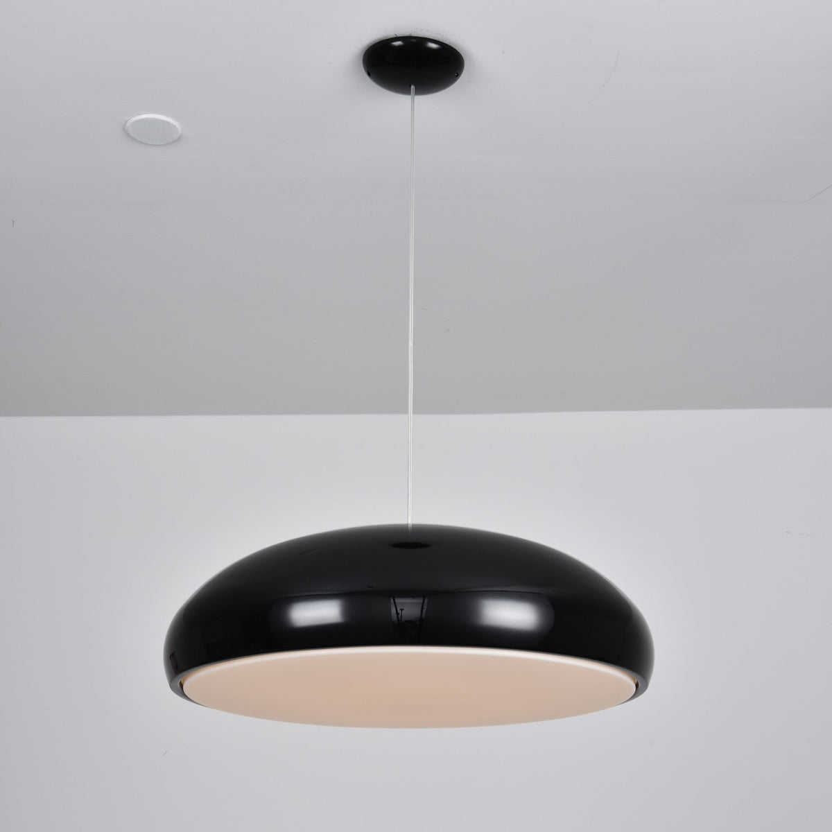 Black Clérachic dome pendant viewed slightly from beneath, with its pale diffuser disc glowing at a low level.