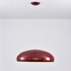 Dark-red Clérachic dome pendant against a pale wall, its glossy shell mirroring the room and its canopy matching the colour.