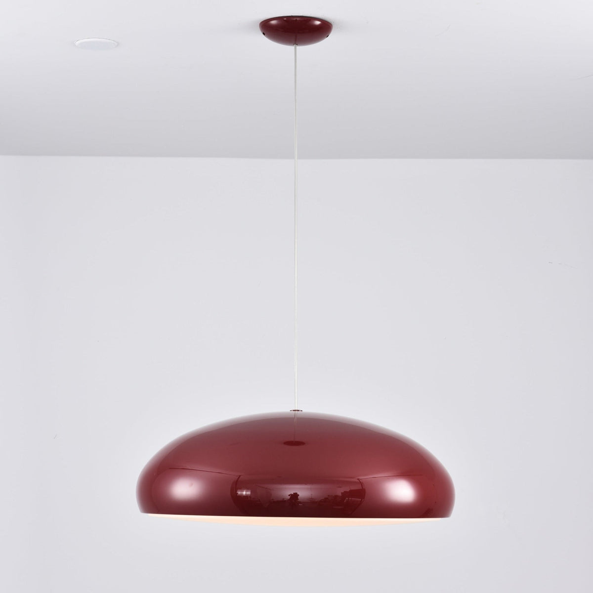 Dark-red Clérachic dome pendant against a pale wall, its glossy shell mirroring the room and its canopy matching the colour.