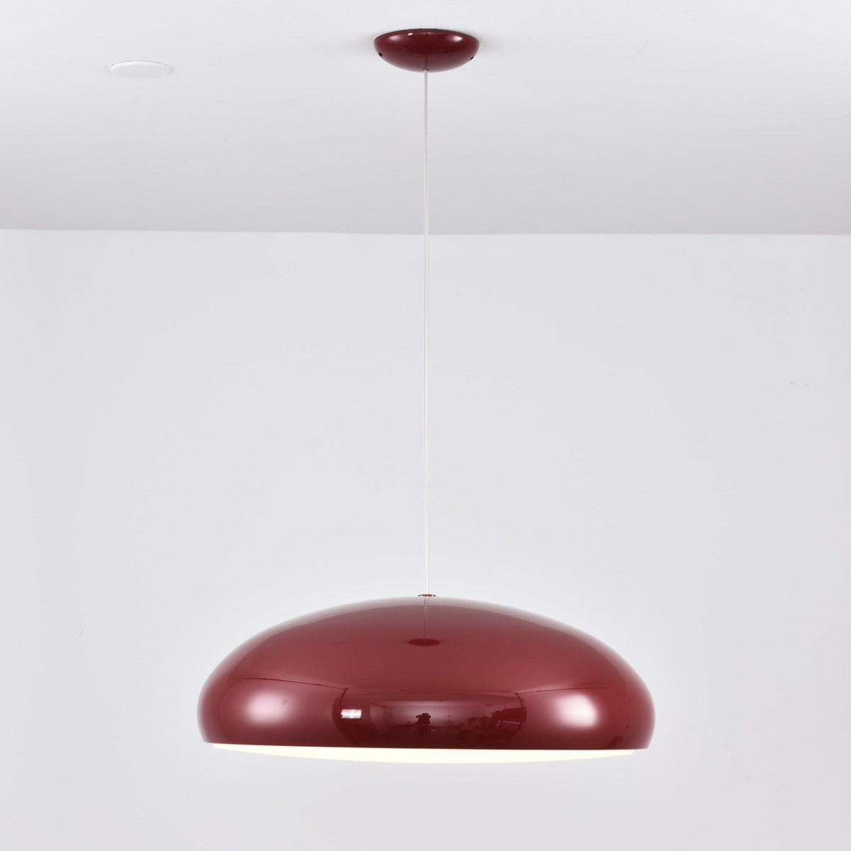 A dark-red Clérachic dome pendant at eye level, unlit, with a glossy shell and a fine white cable.