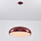Dark-red Clérachic dome pendant lit from below, the round diffuser glowing a warm cream inside its dark rim.
