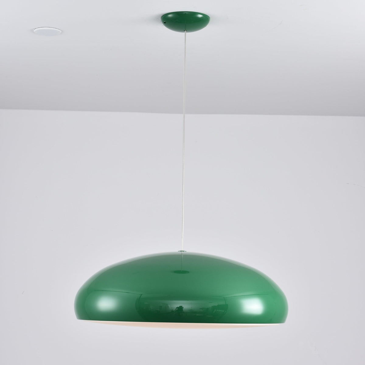 A green Clérachic dome pendant with a glossy shell and a faint warm light under the rim, hung by a thin white cable.