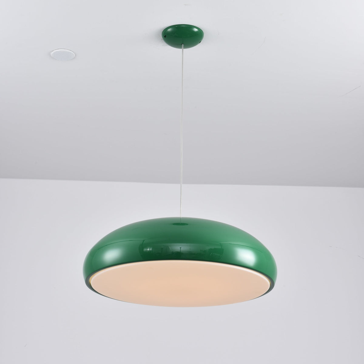 Green Clérachic dome pendant lit from below, the diffuser glowing warm cream inside a dark-green rim.