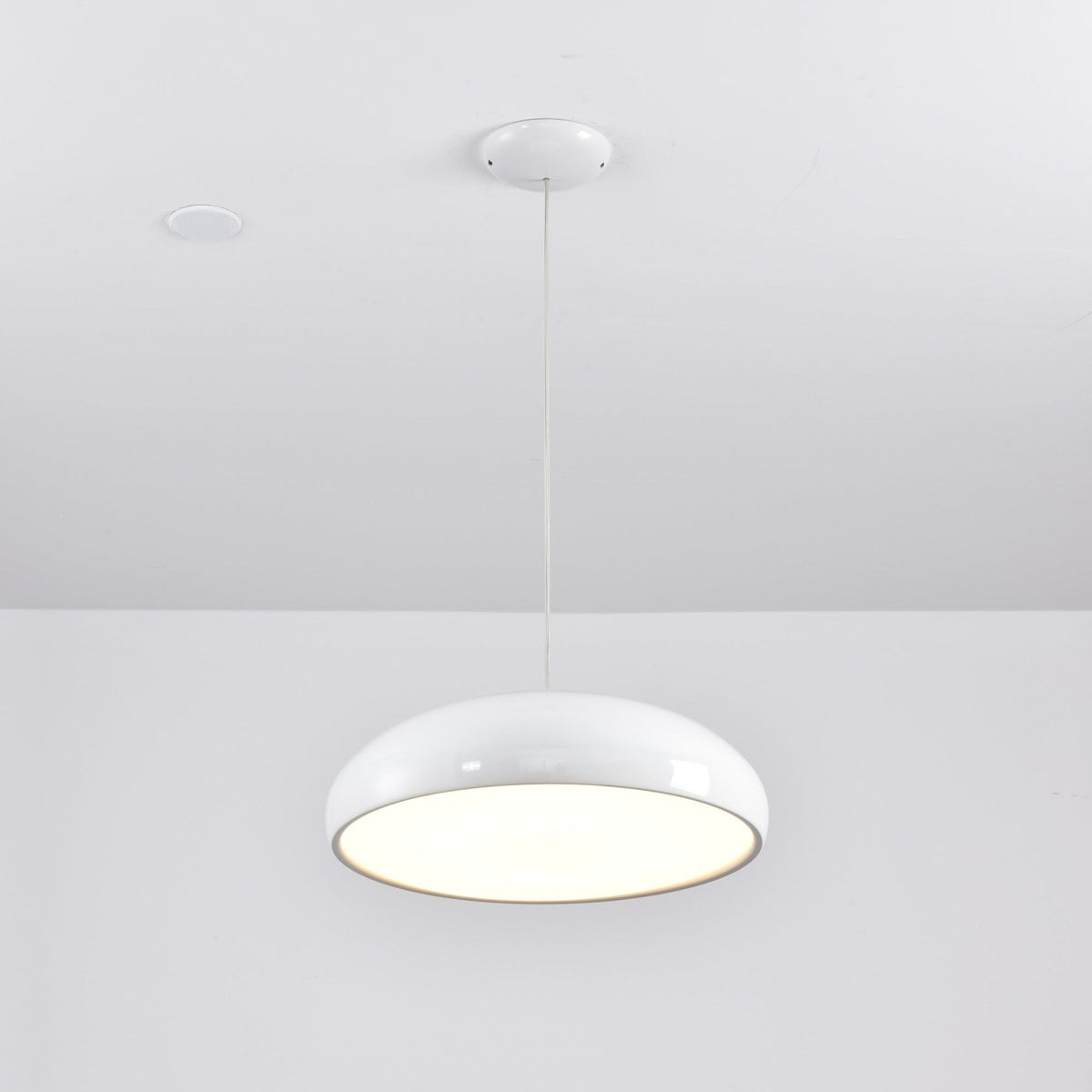 White Clérachic dome pendant seen from below with its diffuser glowing, hung from a white ceiling canopy.