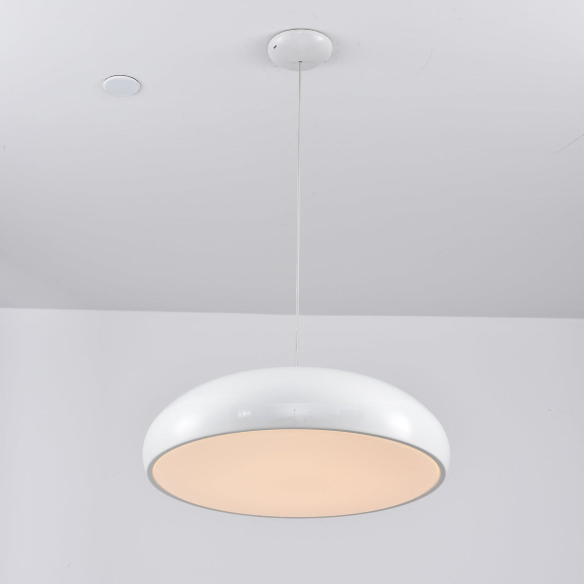 White Clérachic dome pendant lit from below, the diffuser glowing a warm peach inside its glossy rim.