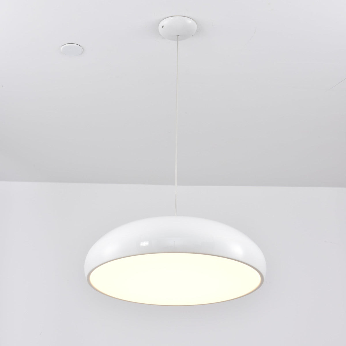 A white Clérachic dome pendant with a bright cream diffuser, hung from a white canopy under a white ceiling.