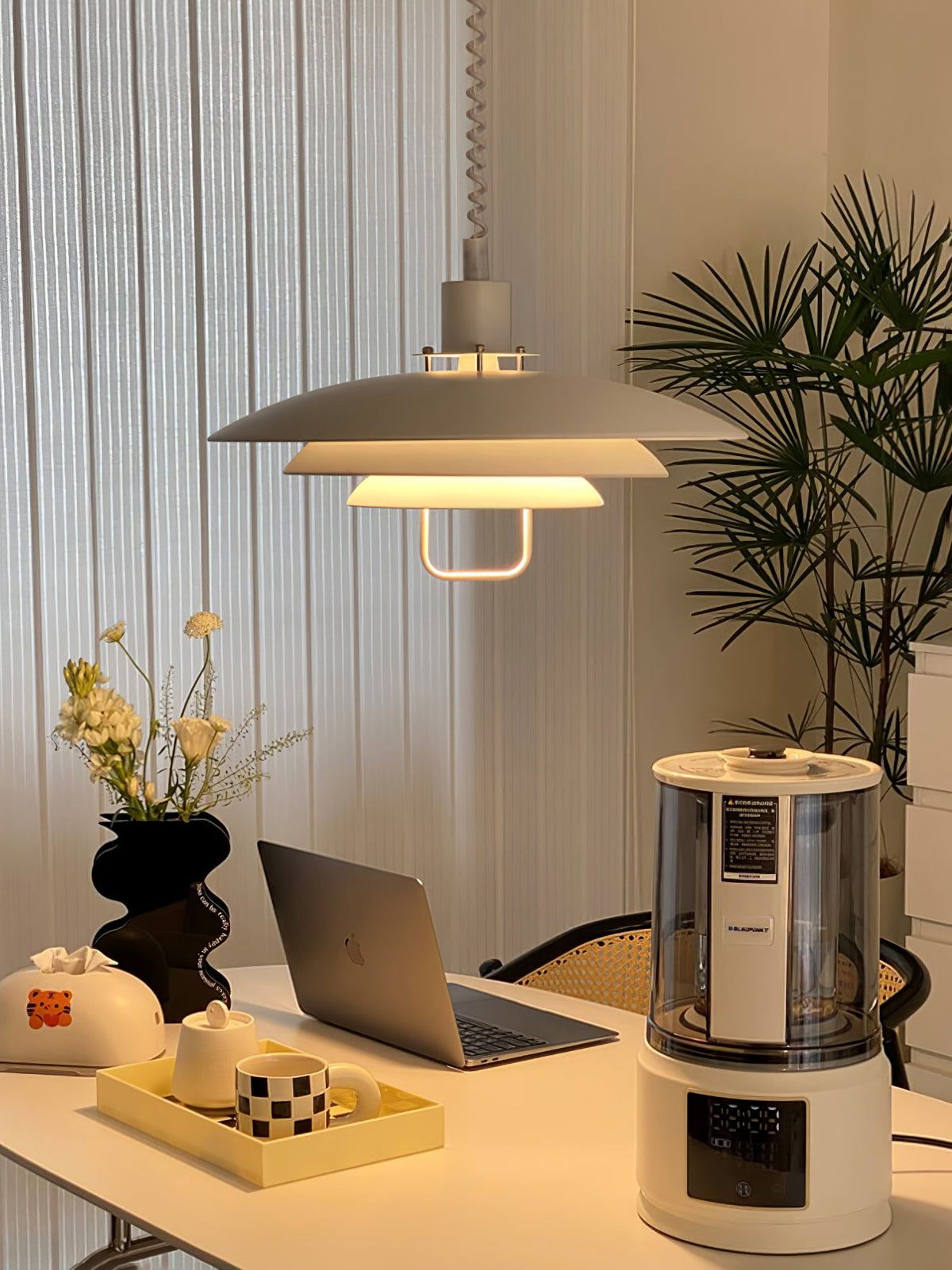 Warm light spills from the lower tiers of this Clérachic pendant, hung over a work table with a laptop and a tray of cups.