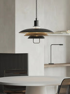 A black Clérachic pendant with tan inner shades hangs beside a pale plaster wall, above a round grey table.