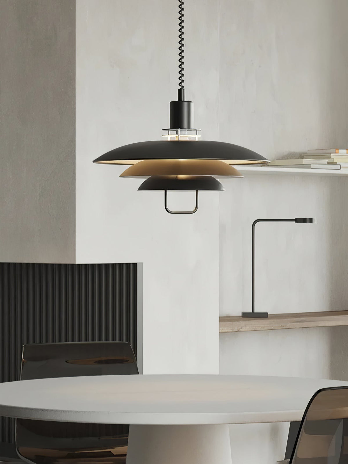 A black Clérachic pendant with tan inner shades hangs beside a pale plaster wall, above a round grey table.
