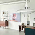 White Clérachic pendant with a chrome-finish collar, seen across a living room with wooden shelves and a wall screen.