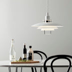 Over a white table holding oil, vinegar and a board of herbs, a white Clérachic pendant hangs near black bentwood chairs.