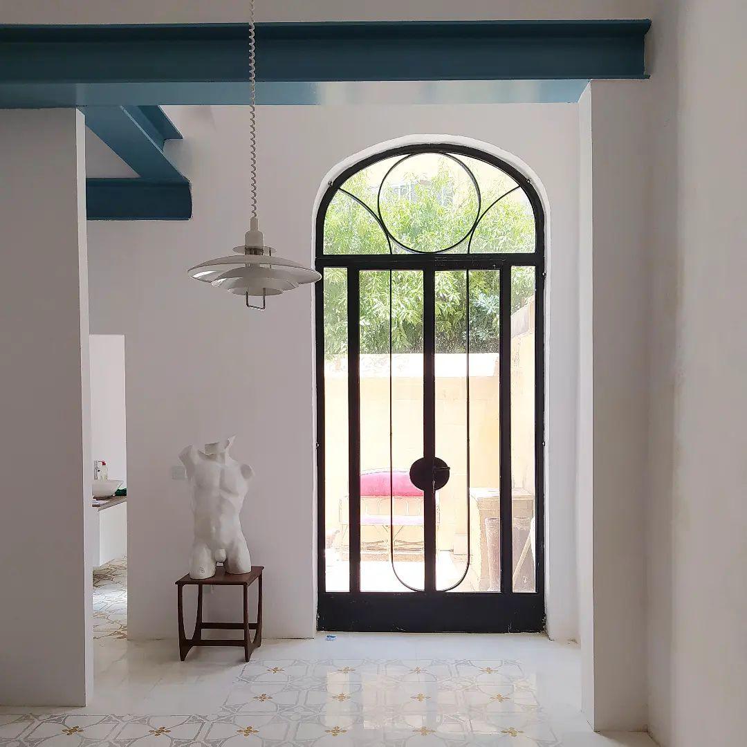 A small white Clérachic pendant hangs in a hallway, in front of an arched black glazed door and a plaster bust.