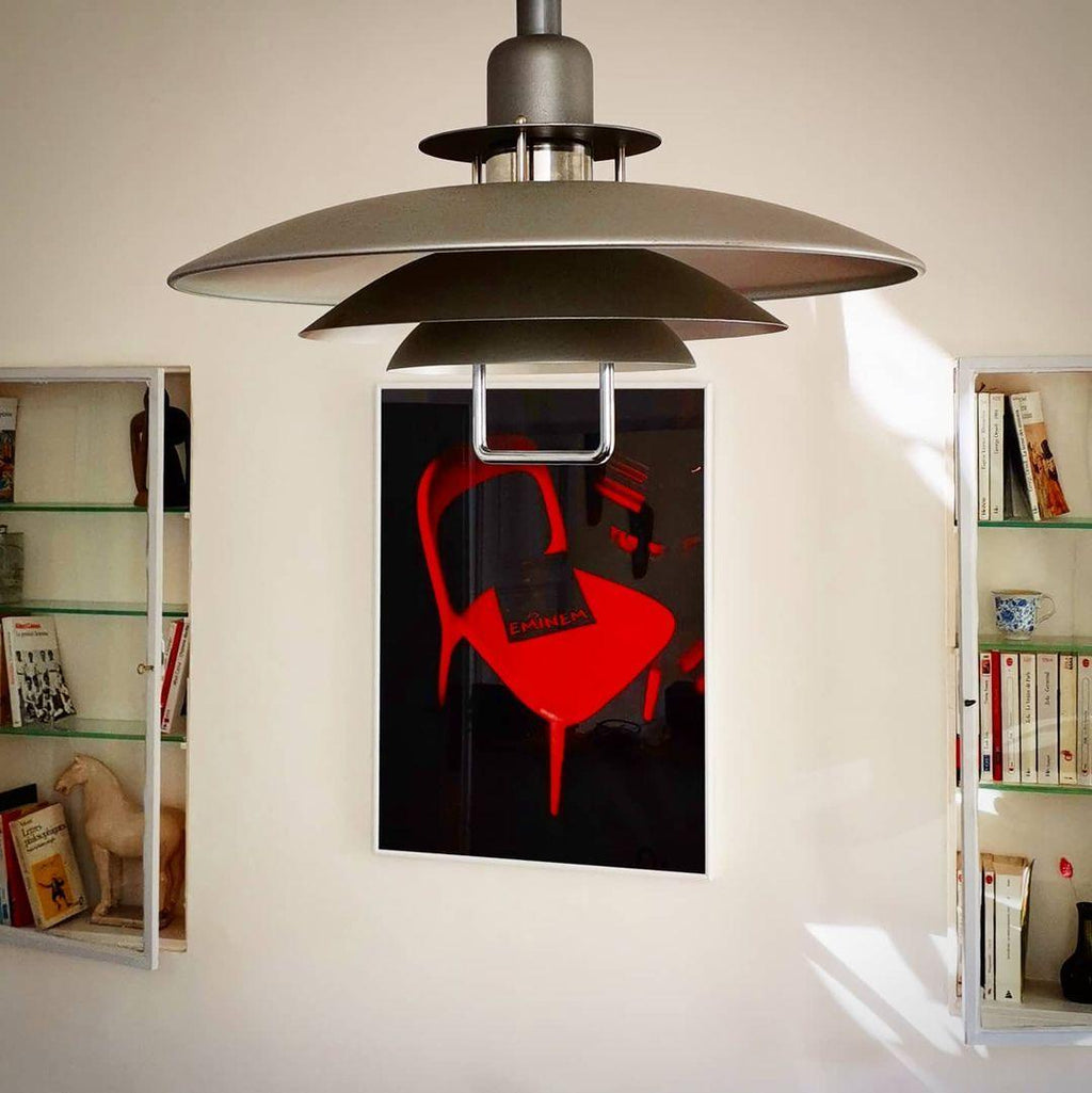 Close view of the dark metal tiers on this Clérachic pendant, hanging in front of a red chair print and built-in shelves.